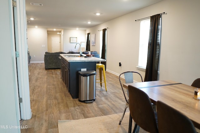 kitchen with a center island with sink, visible vents, light wood-style flooring, a sink, and a kitchen bar