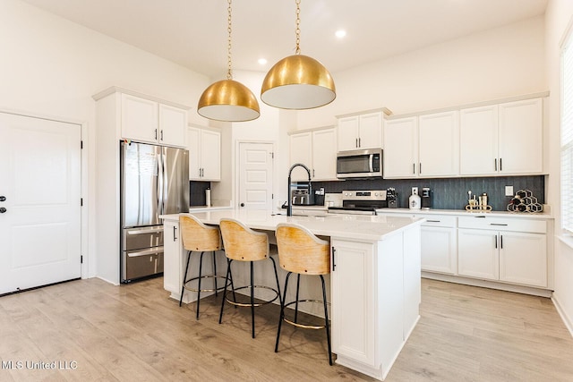 kitchen with stainless steel appliances, an island with sink, light countertops, and white cabinets