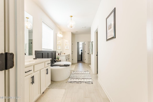 full bath featuring a freestanding bath, wood finished floors, two vanities, and baseboards