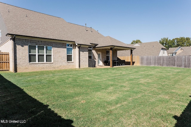 rear view of house with a yard, a fenced backyard, roof with shingles, and brick siding