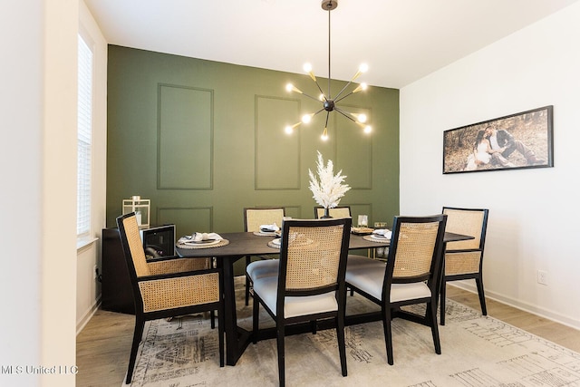 dining room featuring a decorative wall, light wood-style flooring, baseboards, and an inviting chandelier