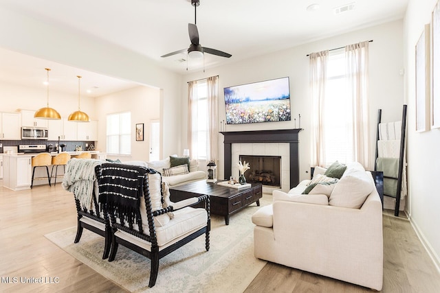 living room featuring light wood finished floors, plenty of natural light, a fireplace, and visible vents