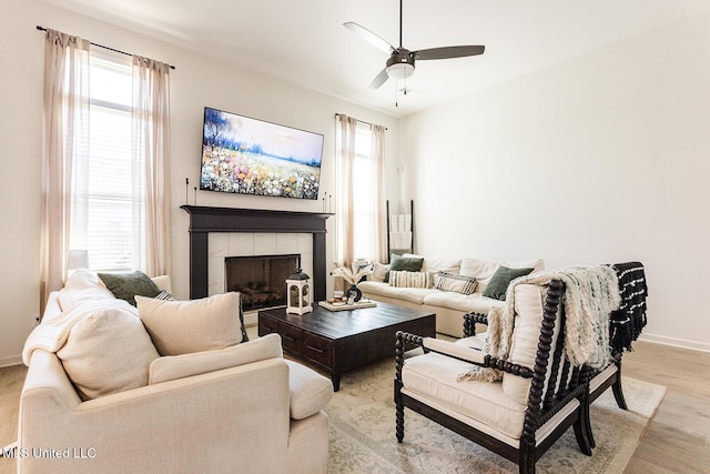 living room featuring a ceiling fan, a fireplace, light wood-style flooring, and baseboards