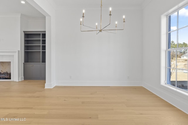 unfurnished dining area featuring ornamental molding, light hardwood / wood-style flooring, an inviting chandelier, and built in shelves