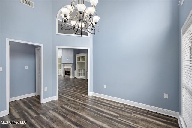 unfurnished dining area featuring dark hardwood / wood-style flooring, a towering ceiling, and a chandelier