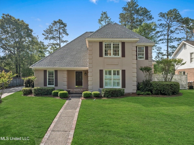traditional-style home featuring fence, stucco siding, a front yard, and roof with shingles