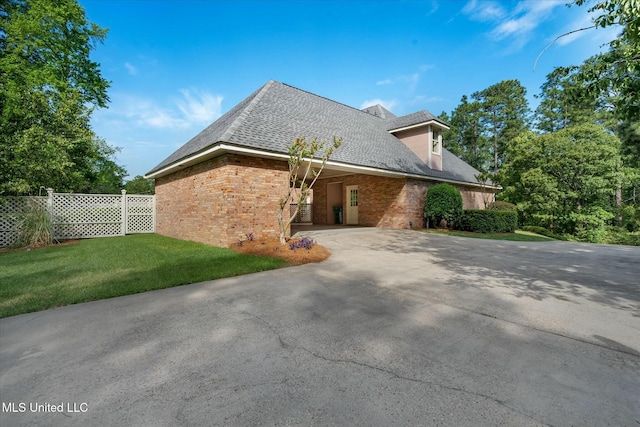 view of side of property with brick siding, fence, driveway, roof with shingles, and a lawn