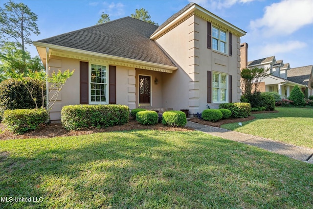 traditional-style home featuring a front yard, stucco siding, and roof with shingles