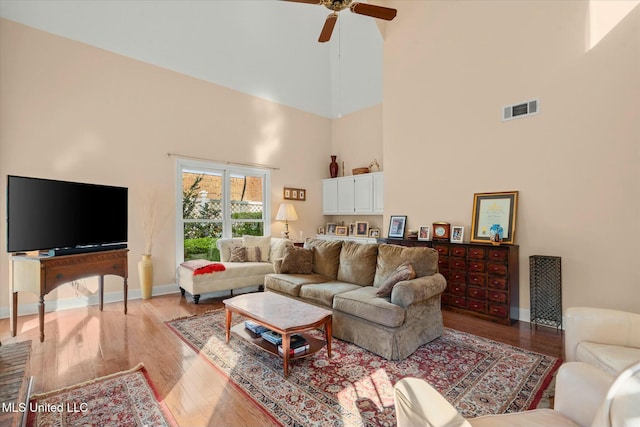 living area with visible vents, ceiling fan, baseboards, light wood finished floors, and a high ceiling