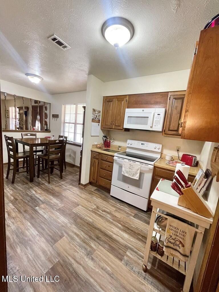 kitchen featuring light wood-type flooring, a textured ceiling, and white appliances