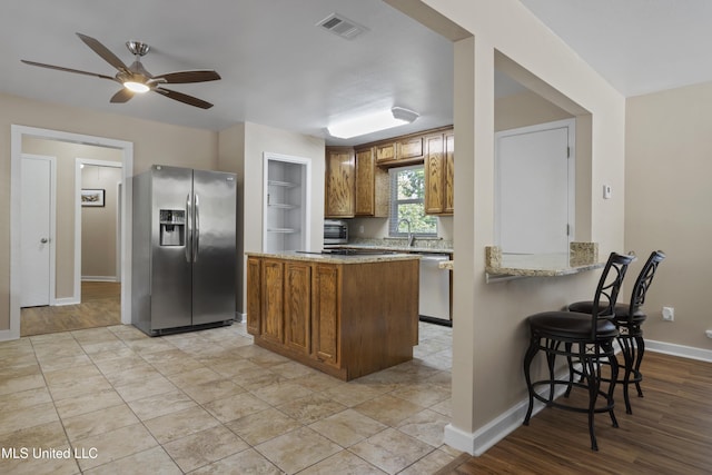 5297 Tuxachanie Dr, Biloxi, MS 39532 - kitchen featuring appliances with stainless steel finishes, brown cabinetry, a ceiling fan, a sink, and light stone counters