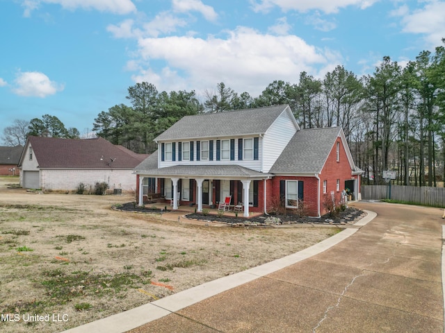 view of front facade featuring a garage, driveway, covered porch, fence, and brick siding