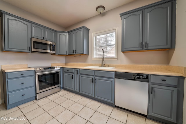 kitchen featuring appliances with stainless steel finishes, light countertops, a sink, and light tile patterned floors