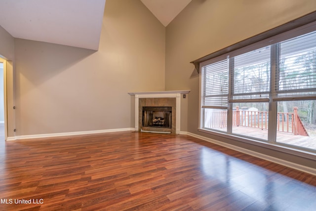 unfurnished living room featuring high vaulted ceiling, wood finished floors, a tile fireplace, and baseboards