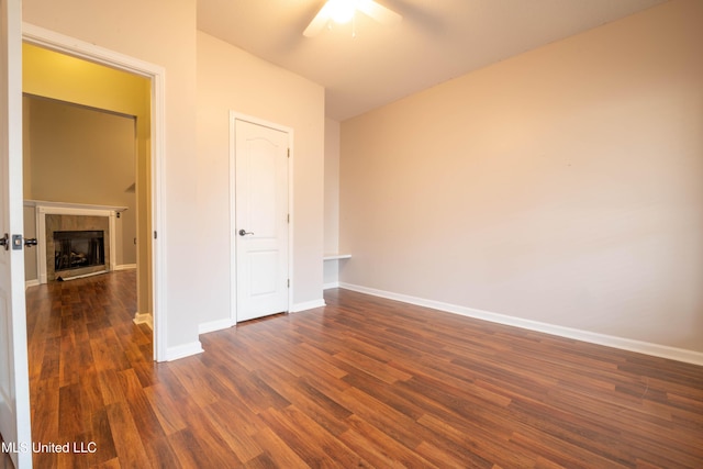 unfurnished bedroom featuring a ceiling fan, dark wood-style flooring, baseboards, and a tiled fireplace