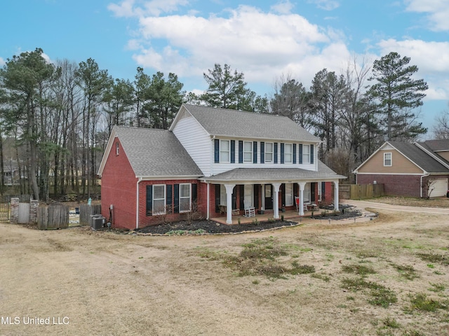 view of front of home with brick siding, a shingled roof, covered porch, fence, and cooling unit