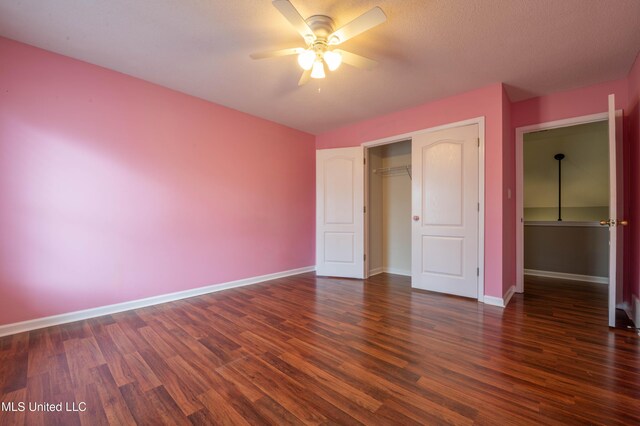 unfurnished bedroom featuring dark wood-style floors, a closet, baseboards, and a ceiling fan