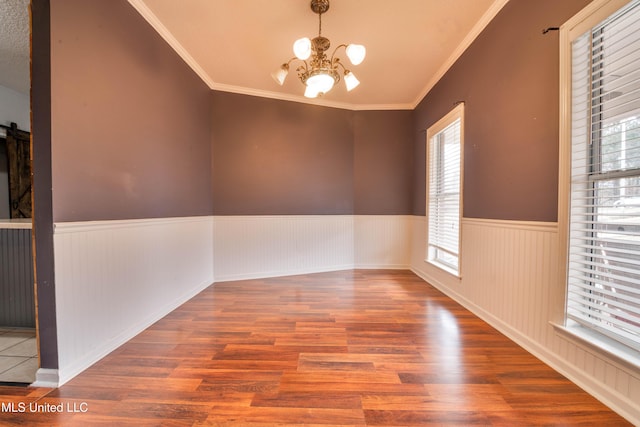 unfurnished room featuring a barn door, a wainscoted wall, ornamental molding, wood finished floors, and an inviting chandelier