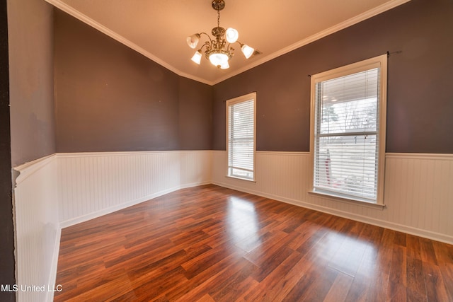 spare room with ornamental molding, wood finished floors, wainscoting, and an inviting chandelier