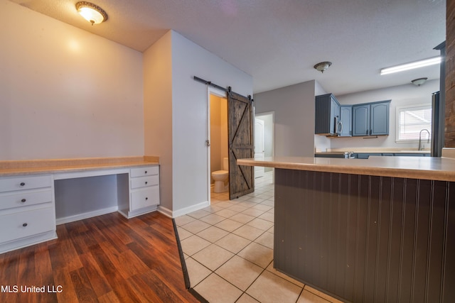 kitchen with a barn door, blue cabinets, light countertops, built in desk, and a sink