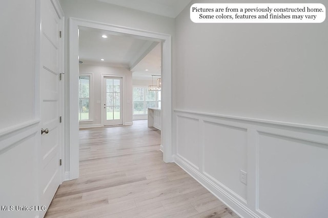 corridor featuring crown molding, a wainscoted wall, a notable chandelier, light wood-style floors, and a decorative wall