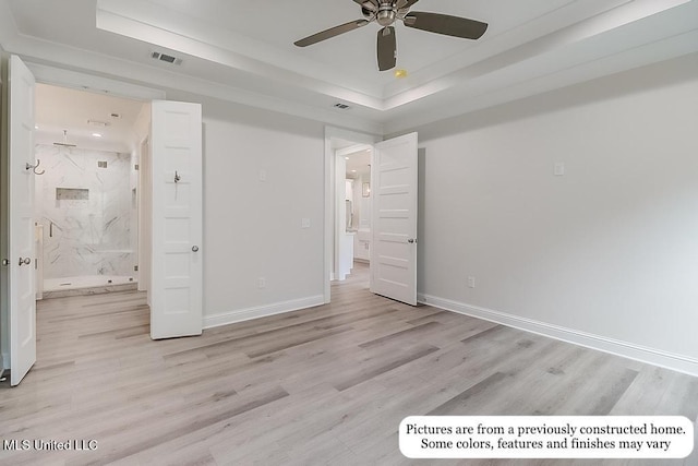 unfurnished bedroom featuring a raised ceiling, light wood-style flooring, baseboards, ensuite bathroom, and visible vents