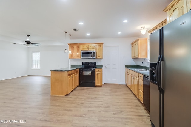 kitchen with a peninsula, a sink, light wood-style floors, black appliances, and dark countertops