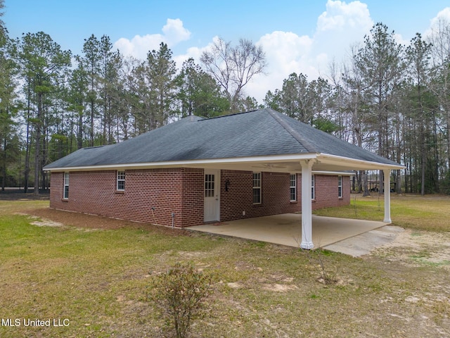 back of property featuring a patio, brick siding, driveway, a lawn, and a carport