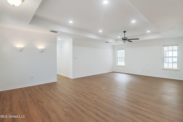 empty room with wood finished floors, a raised ceiling, a ceiling fan, and baseboards