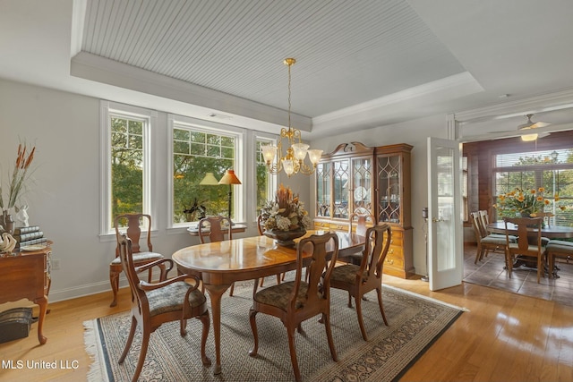 dining area with light hardwood / wood-style floors, ceiling fan with notable chandelier, plenty of natural light, and a tray ceiling