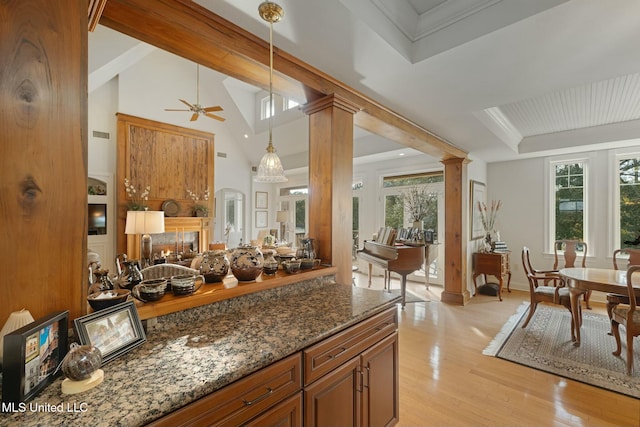 kitchen featuring decorative columns, ceiling fan, dark stone countertops, pendant lighting, and light hardwood / wood-style flooring