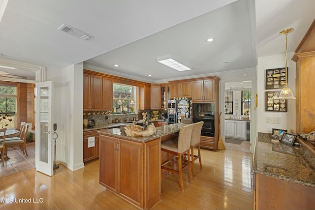 kitchen with a kitchen island, black appliances, light hardwood / wood-style floors, a kitchen breakfast bar, and stone countertops