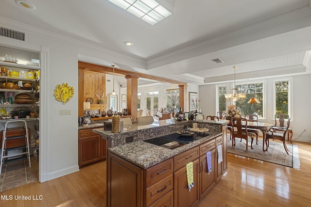 kitchen featuring dark stone countertops, pendant lighting, a kitchen island, black electric cooktop, and decorative columns