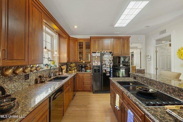 kitchen featuring black appliances, dark stone counters, light hardwood / wood-style floors, sink, and decorative backsplash