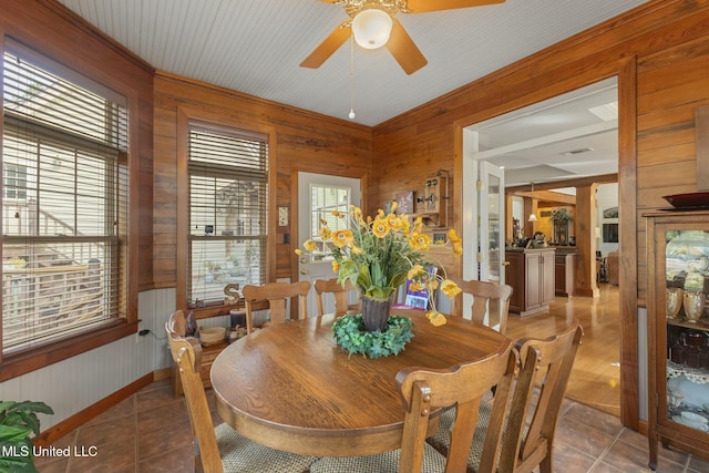 dining room featuring ceiling fan, light tile patterned floors, and wooden walls