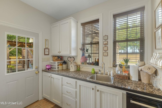 kitchen with stainless steel dishwasher, sink, light tile patterned flooring, white cabinetry, and dark stone counters