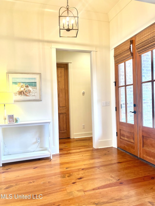 entrance foyer with french doors, ornamental molding, a chandelier, and light hardwood / wood-style floors