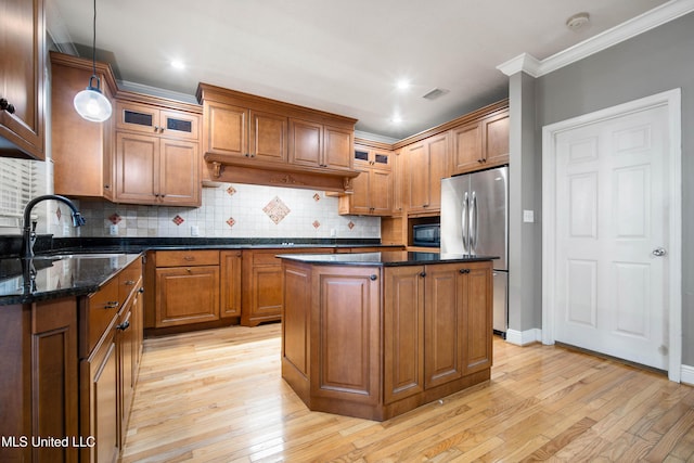 kitchen featuring stainless steel refrigerator, black microwave, a center island, dark stone countertops, and pendant lighting