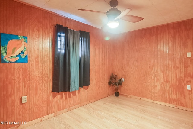 unfurnished room with ceiling fan, wood walls, baseboards, and wood finished floors