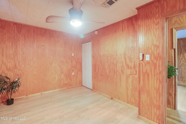 empty room featuring ceiling fan, wooden walls, visible vents, baseboards, and light wood-type flooring