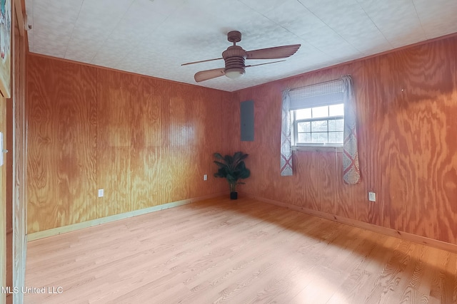 unfurnished room with light wood-style floors, ceiling fan, electric panel, and wood walls