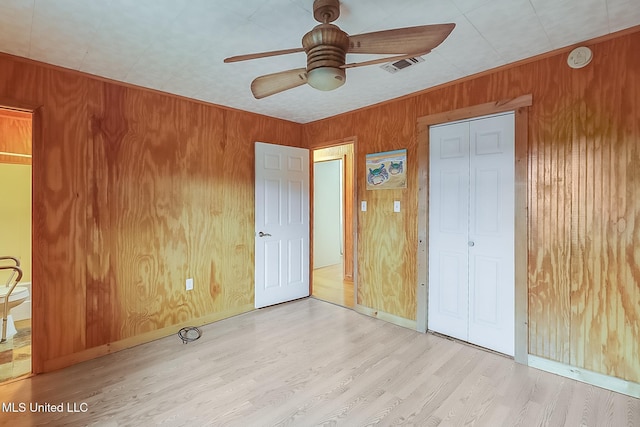 unfurnished bedroom with light wood-style floors, a closet, visible vents, and wood walls