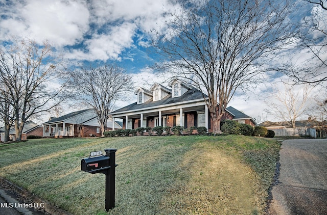 cape cod-style house with covered porch, brick siding, and a front lawn