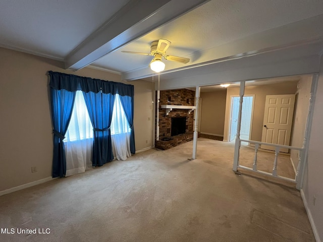 unfurnished living room featuring beam ceiling, ceiling fan, a brick fireplace, carpet floors, and crown molding