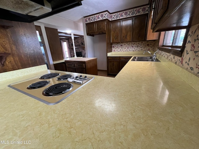 kitchen featuring stainless steel electric stovetop, kitchen peninsula, sink, dark brown cabinetry, and a fireplace