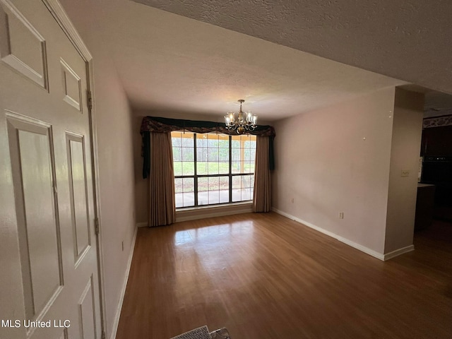 unfurnished dining area featuring a textured ceiling, dark hardwood / wood-style floors, and an inviting chandelier