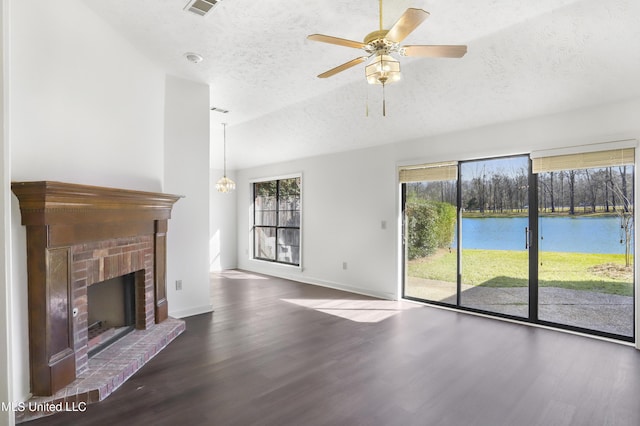 unfurnished living room featuring hardwood / wood-style floors, ceiling fan with notable chandelier, lofted ceiling, a fireplace, and a water view