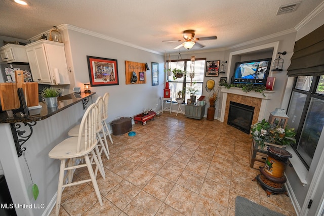 kitchen with a tile fireplace, white cabinetry, a textured ceiling, ceiling fan, and crown molding