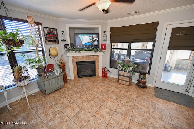 living room featuring tile patterned flooring, a tiled fireplace, ceiling fan, ornamental molding, and a textured ceiling