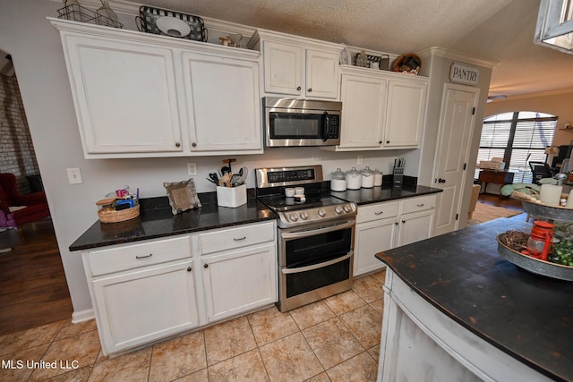 kitchen with appliances with stainless steel finishes, ceiling fan, a textured ceiling, white cabinets, and light tile patterned flooring